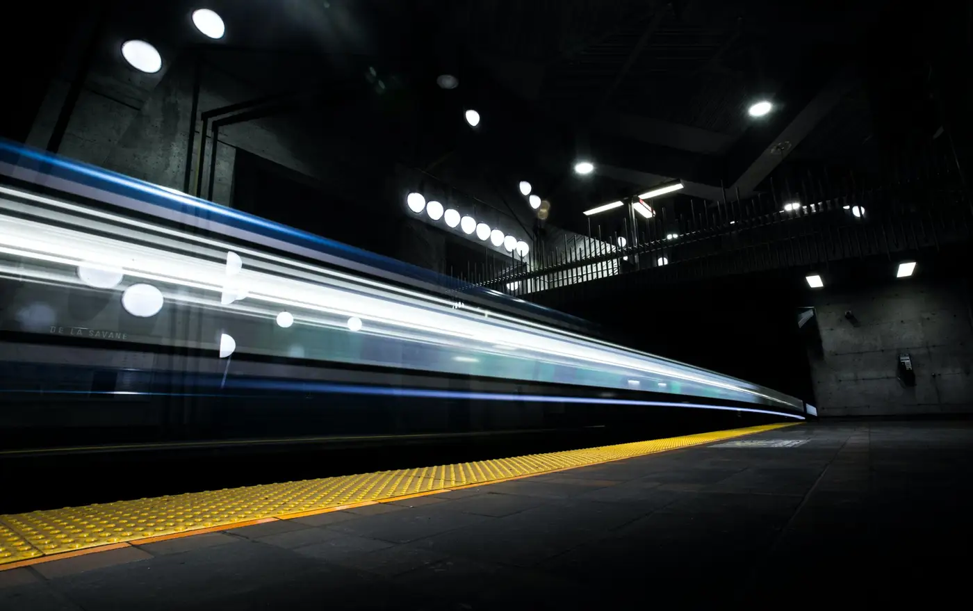 Ein Zug fährt bei Nacht in einen beleuchteten Bahnsteig ein, die Lichter ziehen Spuren