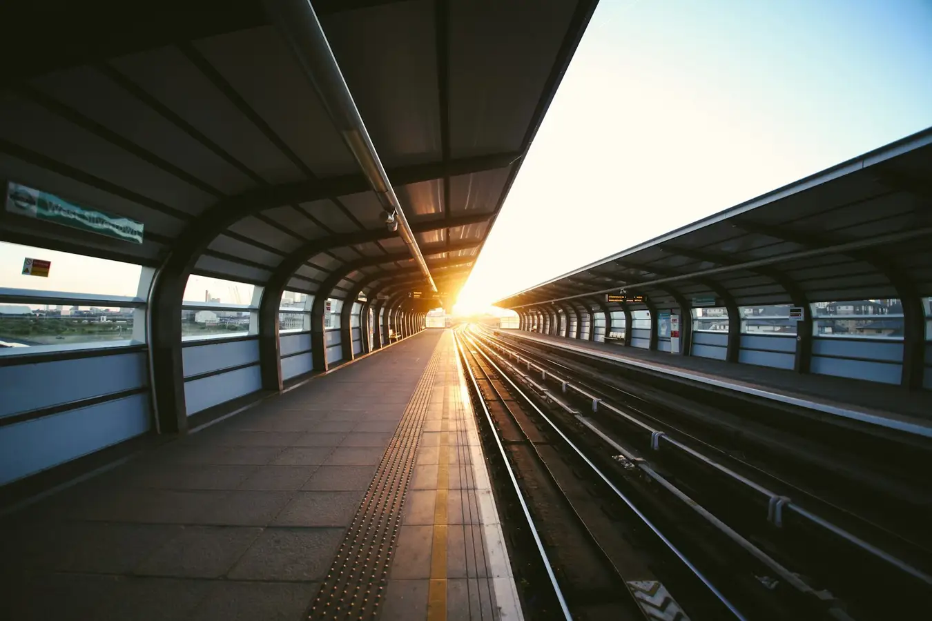 Bahnsteig mit Gleisen, die im Gegenlicht auf einen Fluchtpunkt zulaufen