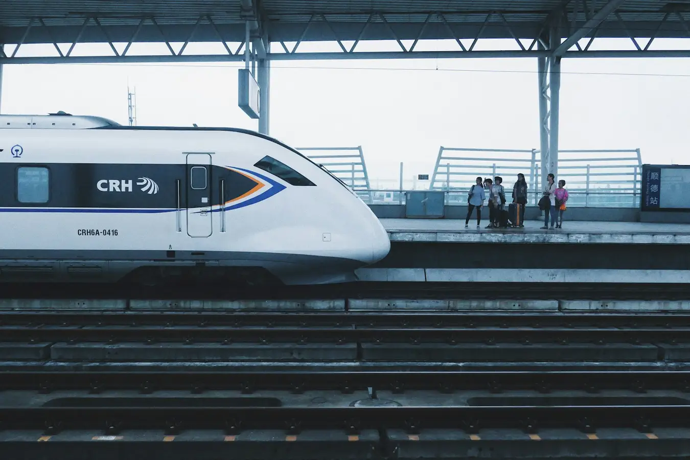 Weißer Hochgeschwindigkeitstriebzug an einem Bahnsteig, im Hintergrund wartende Reisende