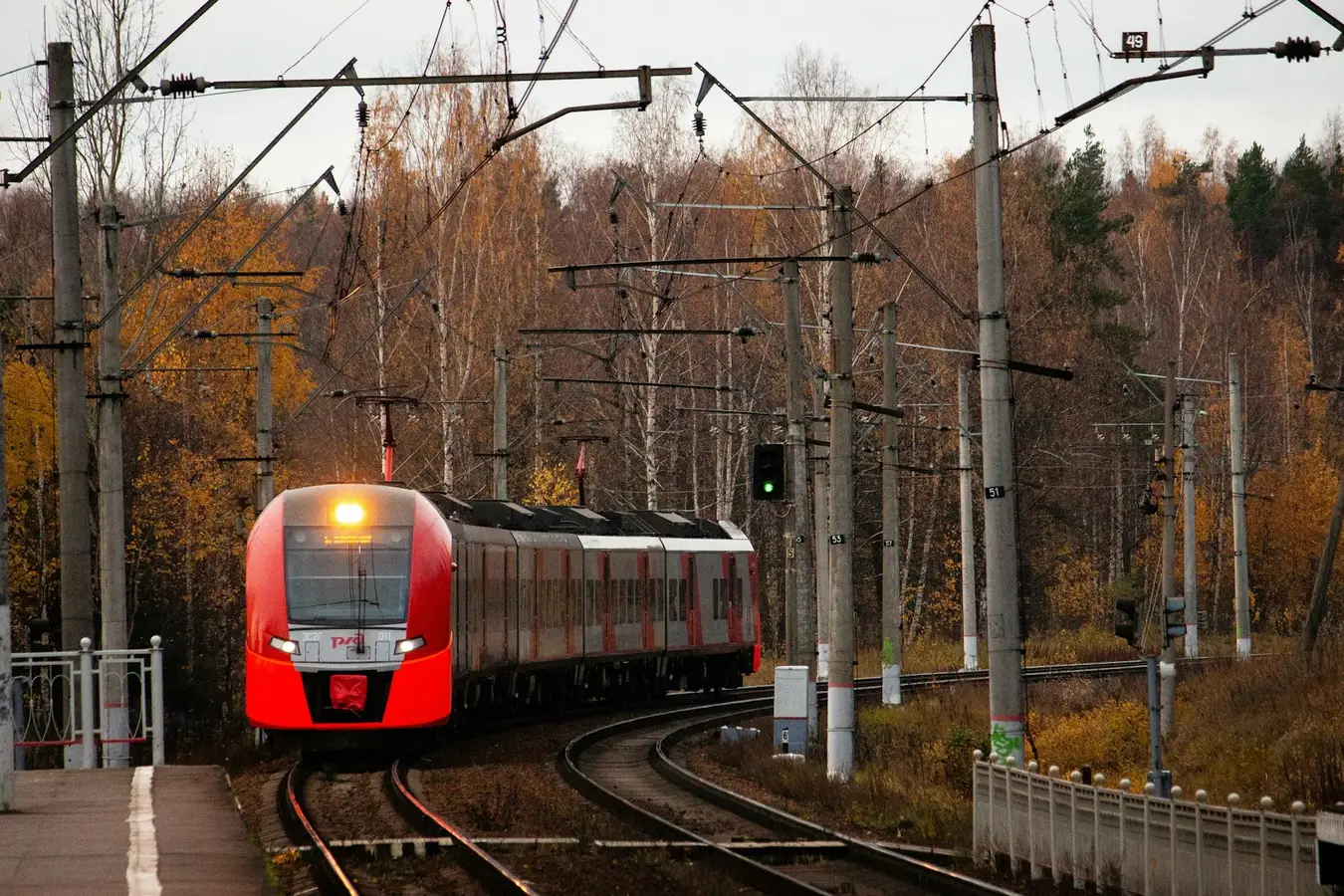 Roter Regionaltriebzug auf elektrifizierter Strecke, Oberleitungsmasten und Signale im Bild